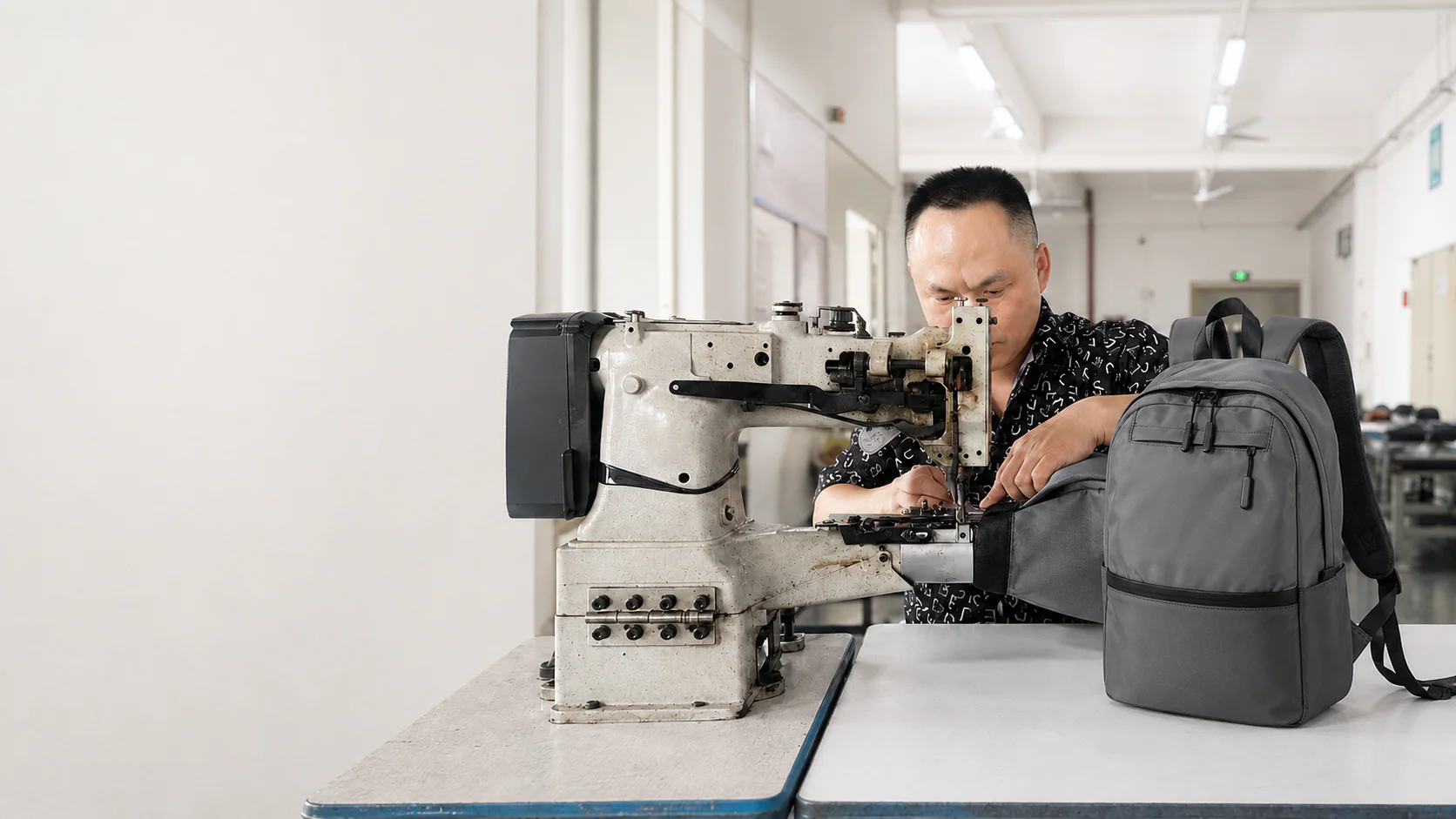 Heavy-duty sewing and finished custom backpack production at Hongzhao Hongzhao sewing operator finishing a gray custom business backpack on a heavy-duty post-bed sewing machine
